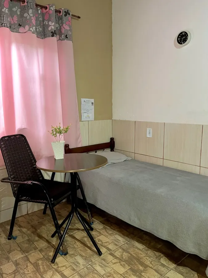 Quarto individual com cama, mesa de apoio e cortina na janela