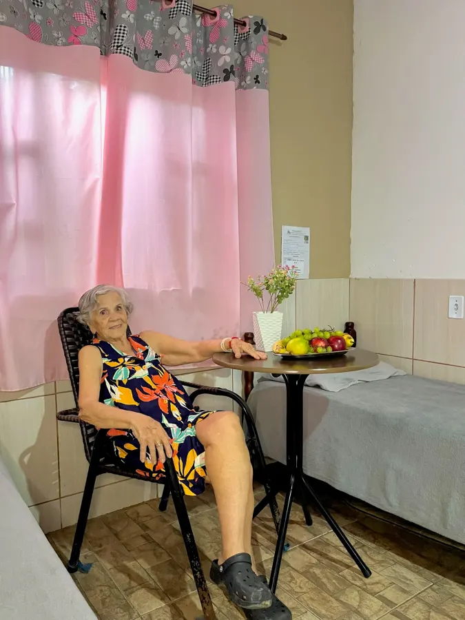 Residente sentada em seu quarto individual, com fruteira sobre a mesa